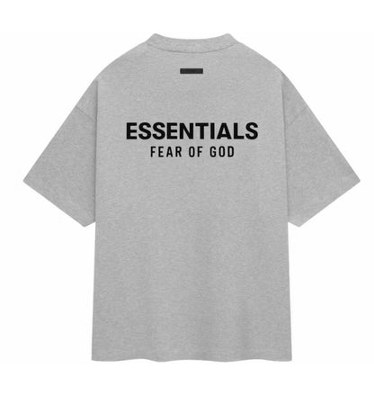 A light gray heather short-sleeve t-shirt with 'ESSENTIALS' and 'FEAR OF GOD' printed in black on the back, shown against a plain white background.